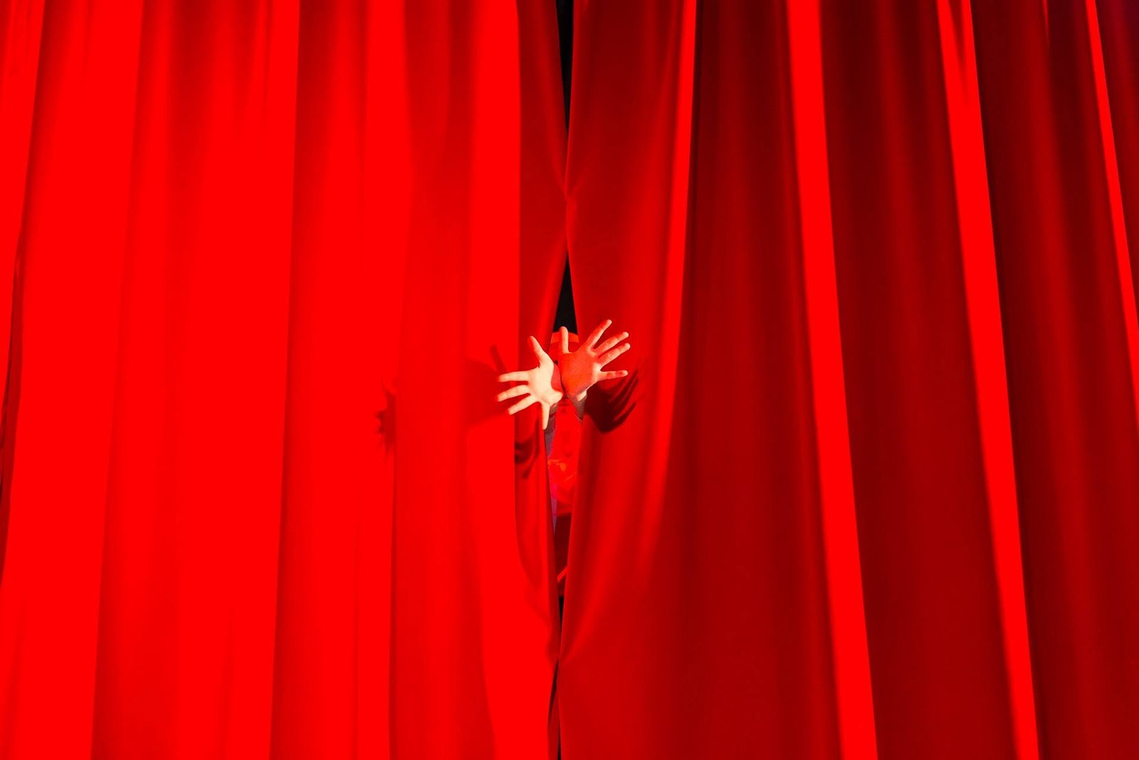 Un sipario rosso chiuso, e due mani che spuntano in mezzo