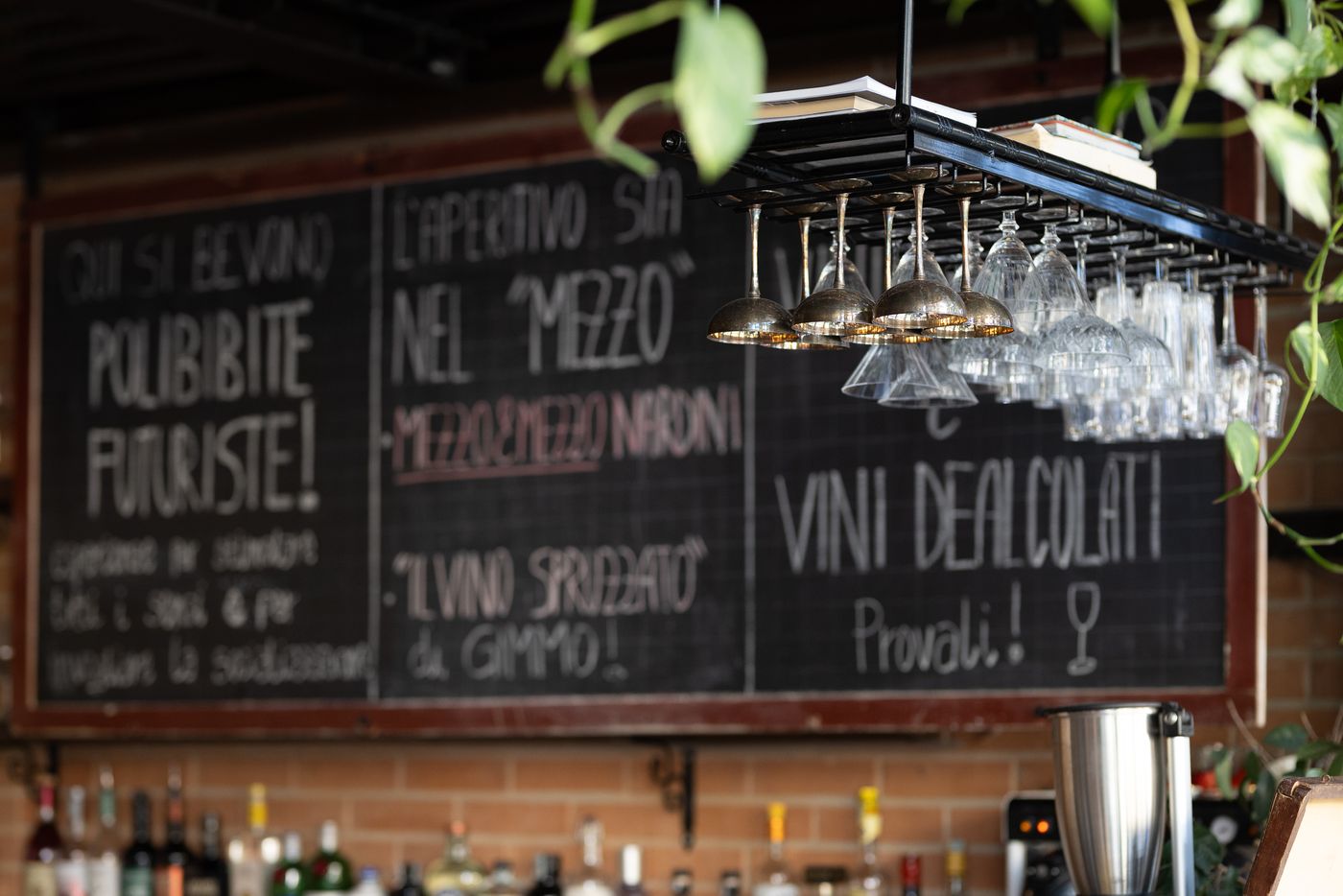 Il bancone del Renny: bottiglie, bicchieri appesi e le lavagne con i cocktail scritti a mano.