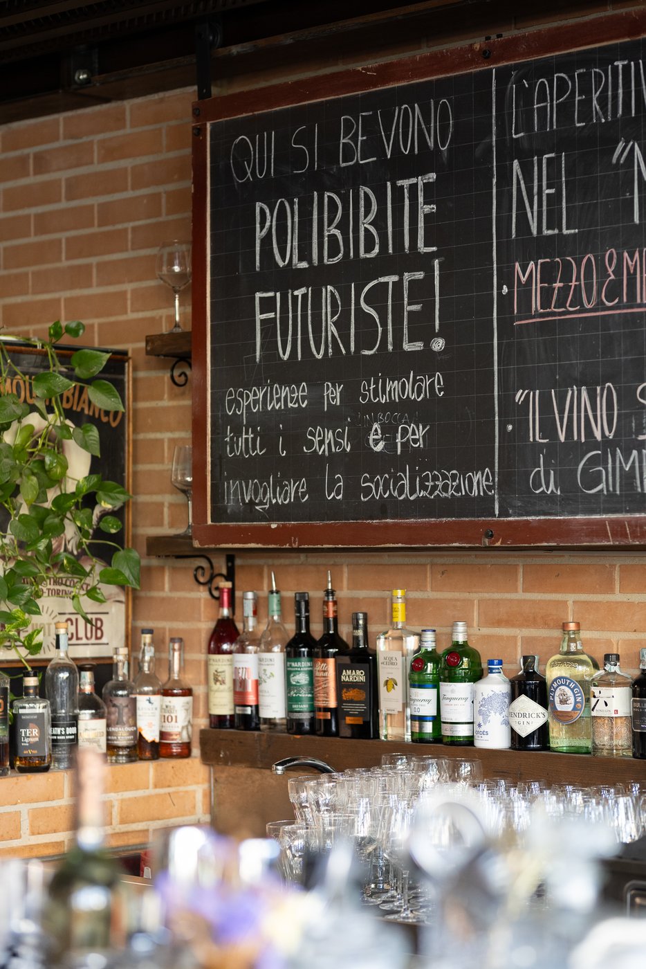 La lavagna del bancone — «Qui si bevono polibibite futuriste!» — e sotto la mensola con le bottiglie.